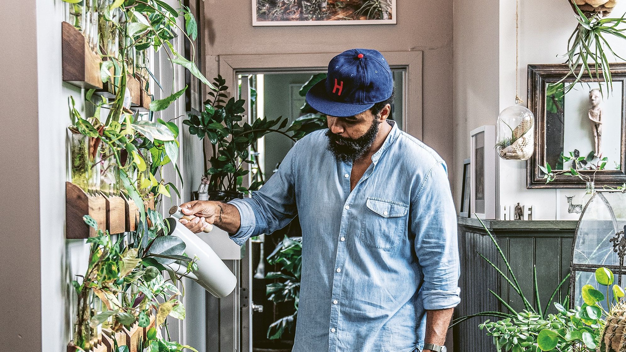 Hilton Carter tending watering a living wall of plants in his apartment hallway