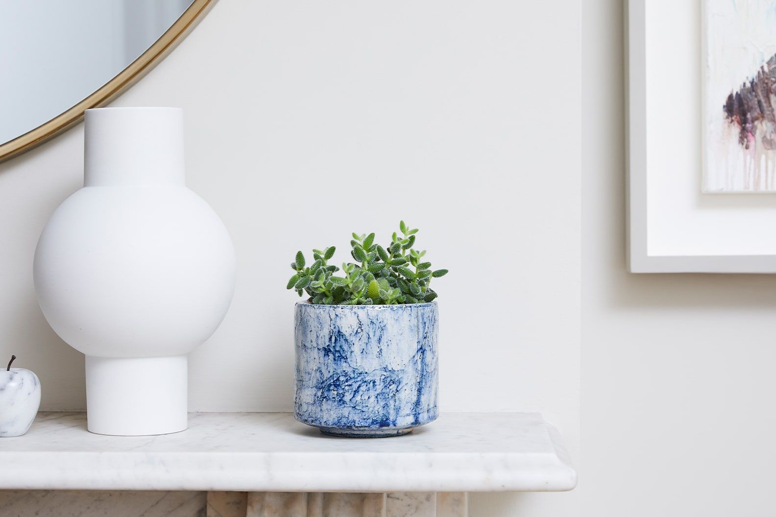 A pickle plant in a blue fractured decorative pot on a mantlepiece in a living room