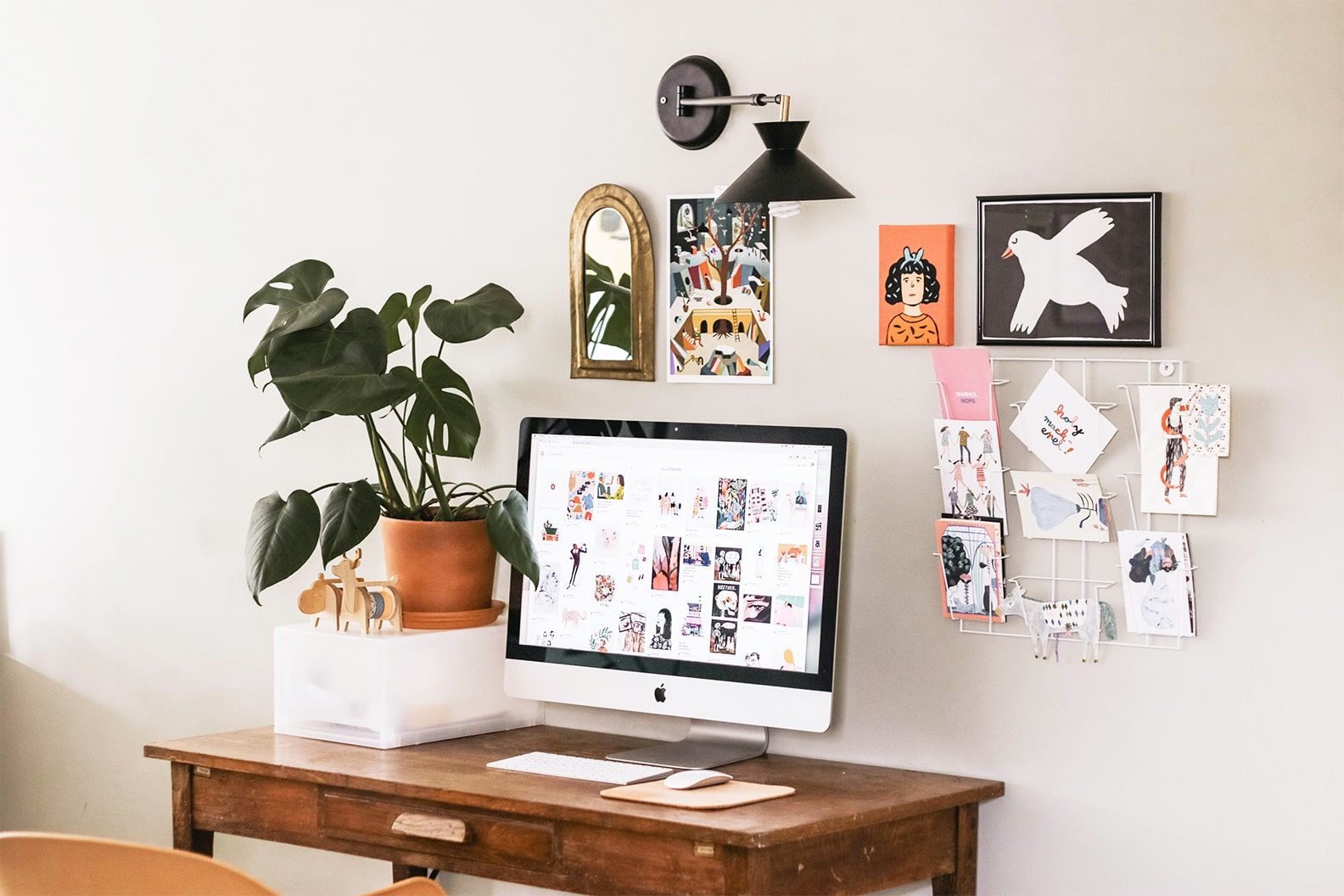 A small swiss cheese plant in a teracotta pot sits on a desk, next to a laptop