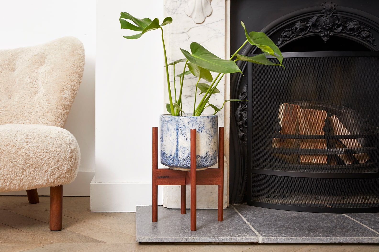 A monstera in a blue fractured ceramic pot in a plant stand in a living room