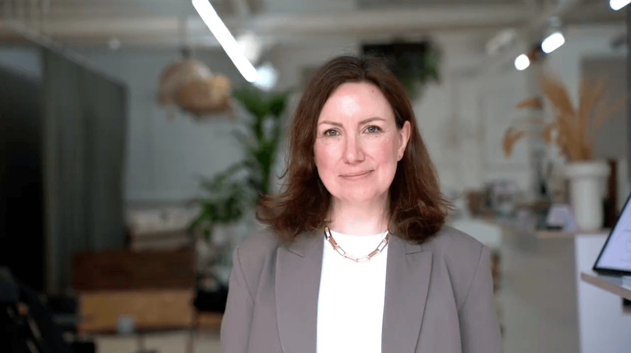 Emily Wheeler wears a white T-shirt and a khaki blazer, and is smiling at the camera
