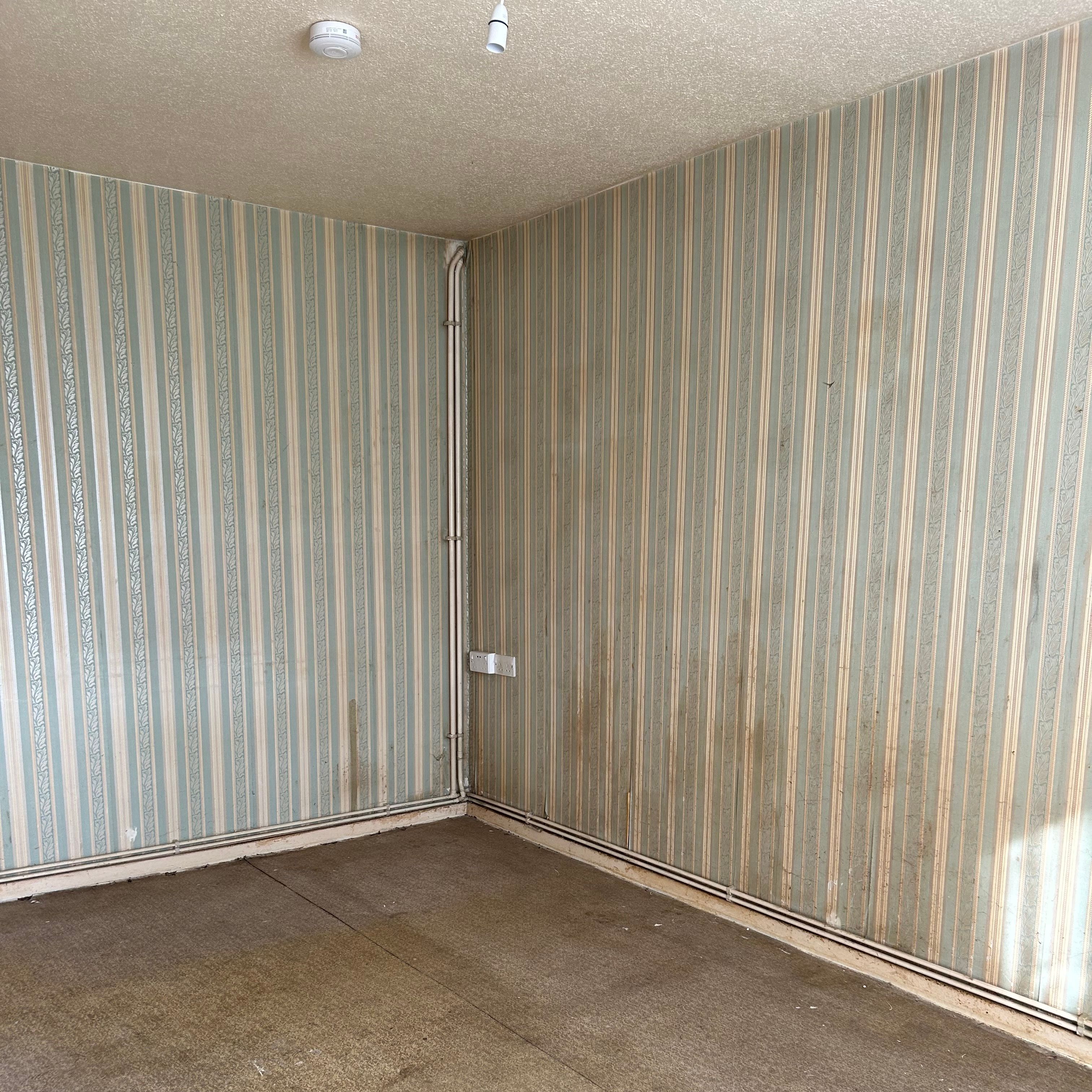 A room with old, dirty wallpaper and no flooring