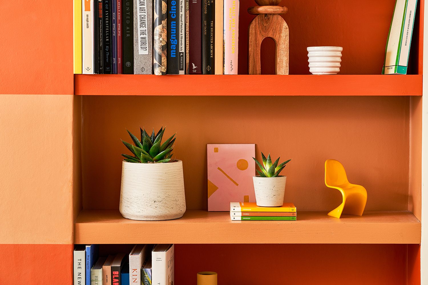 Two succulents in white clay pots sit in a terracotta shelving unit decorated with books