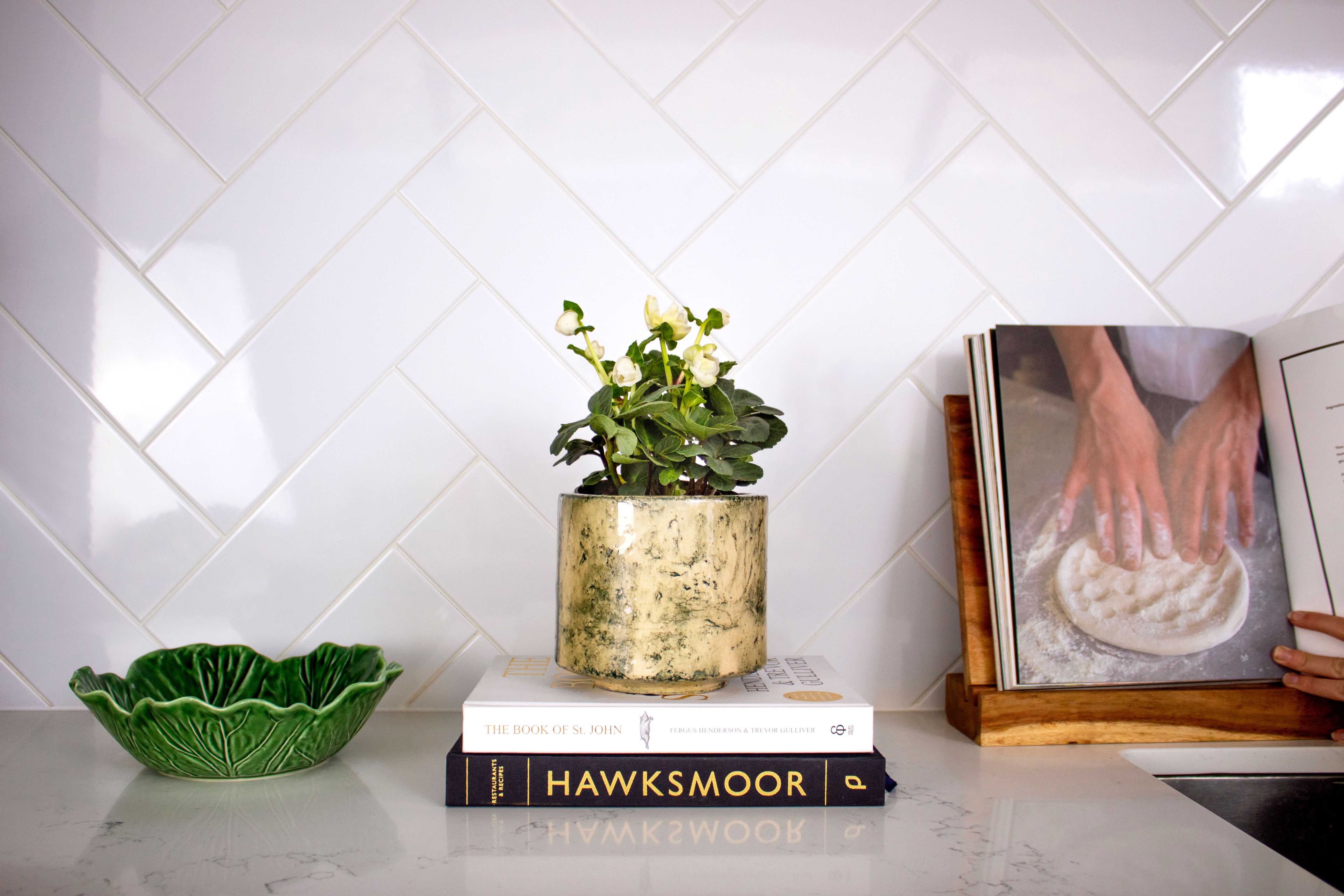 A white helebore plant sits on a stack of books on a kitchen worktop