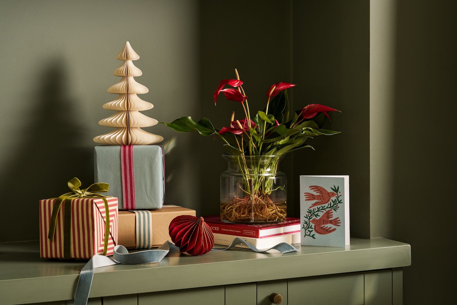 A red hydroponic Anthurium is surrounded by gifts and paper baubles