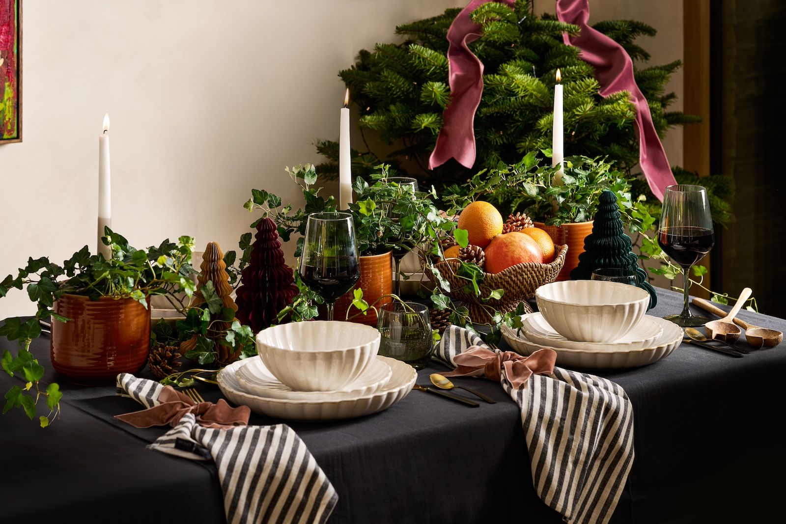 A Christmas table set with English ivy, striped napkins, paper Christmas trees and candles.