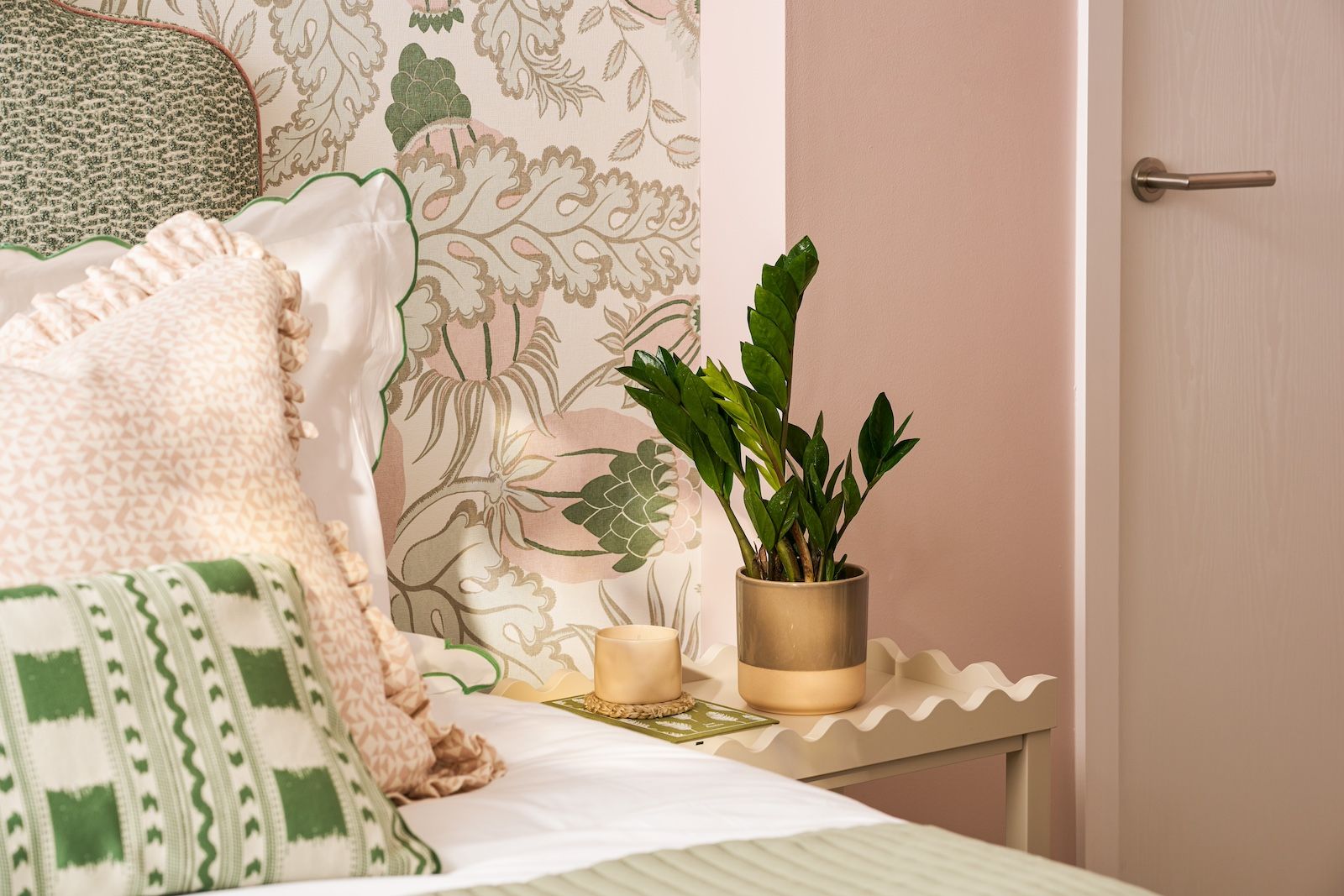 A pink and green bedroom with a ZZ plant on the side table